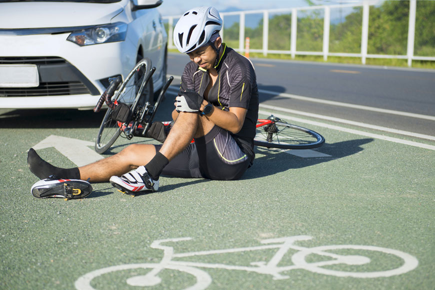 An injured cyclist sits on the ground in a separated bike line after an accident