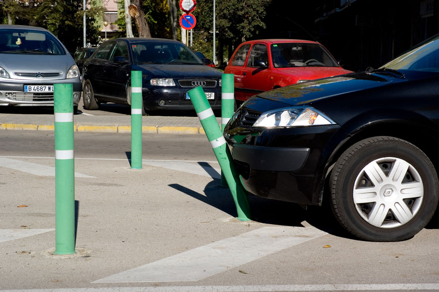 A green flex post bends under the bumper of a black car