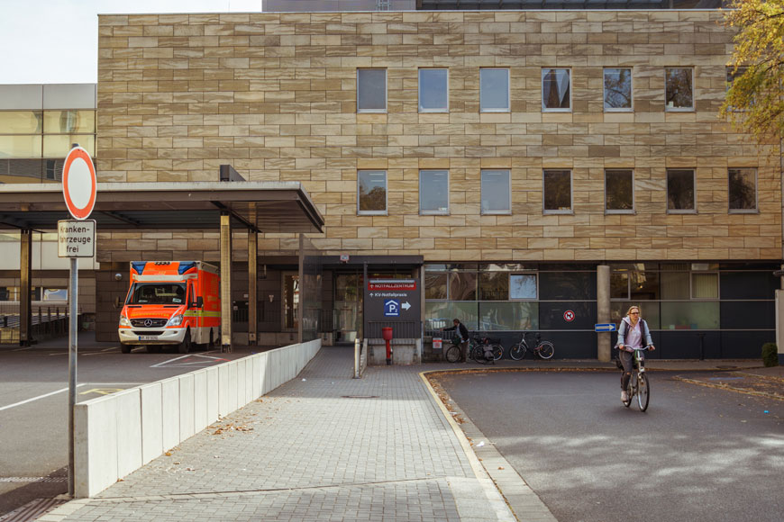 A woman on a bicycle is separated from the ambulance dock by a small retaining wall