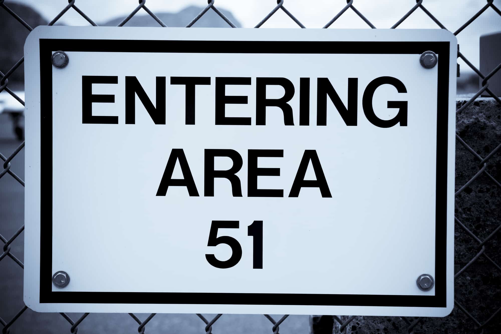 Sign on a chain link fence reading Entering area 51